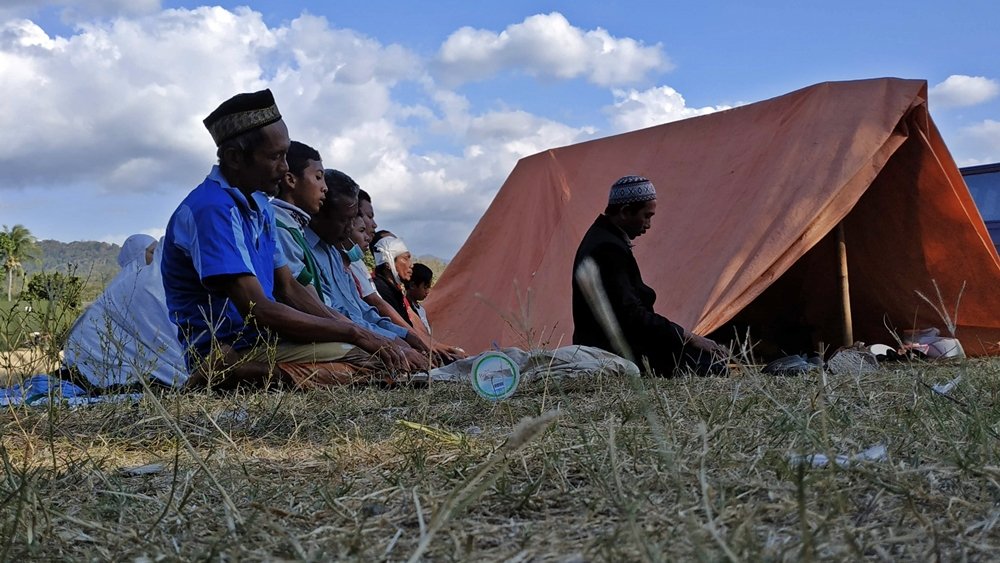 Warga melaksanakan salat di dekat tenda pengungsian saat rangkaian gempa Lombok 2018. Gempa susulan yang terus terjadi membuat banyak warga bertahan di ruang terbuka selama berhari-hari. Foto: Arsip kicknews.today