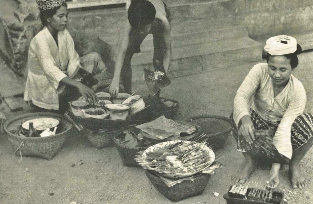 Seorang perempuan memasak sate di Ampenan, Lombok, dalam foto yang diterbitkan pada 1953 melalui buku Wanita di Indonesia/Women in Indonesia. Foto: Stoomvaart Maatschappij Nederland/Wikimedia Commons.