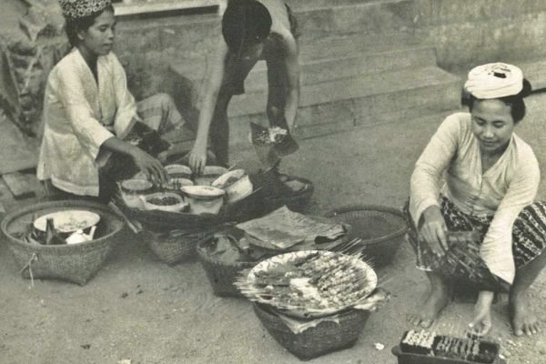 Seorang perempuan memasak sate di Ampenan, Lombok, dalam foto yang diterbitkan pada 1953 melalui buku Wanita di Indonesia/Women in Indonesia. Foto: Stoomvaart Maatschappij Nederland/Wikimedia Commons.