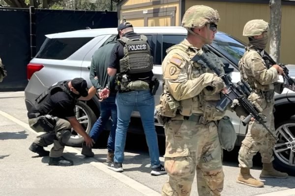 Petugas polisi menahan seseorang di dekat anggota Garda Nasional di sebuah lokasi yang disebut berada di Los Angeles, California, Amerika Serikat, dalam gambar siaran pers yang dirilis pada 10 Juni 2025. (REUTERS)